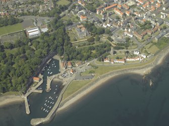 Oblique aerial view centred on the harbour with the monastery, garden, church, churchyard and burial ground adjacent, taken from the SSE.