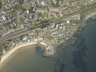 Oblique aerial view centred on the church, burial ground and harbour, taken from the S.