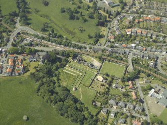 Oblique aerial view centred on the remains of the castle, dovecot and walled garden and the church and burial-ground, taken from the SE.
