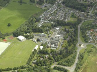 Oblique aerial view centred on the school, church, hospital and house, taken from the NW.