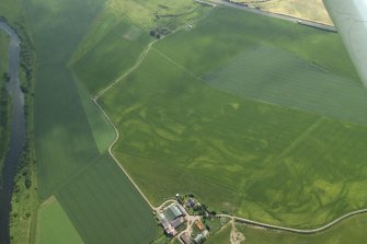 Oblique aerial view centred on the cropmarks of the rig, pits and possible barrows with the cropmarks of the enclosure and ring-ditches and the farmhouse and farmsteading adjacent, taken from the NW.