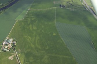 Oblique aerial view centred on the cropmarks of the rig, pits and possible barrows with the cropmarks of the enclosure and ring-ditches and the farmhouse and farmsteading adjacent, taken from the WSW.