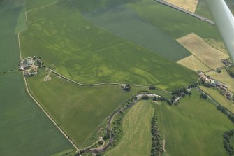 Oblique aerial view centred on the cropmarks of the rig with the cropmarks of the rig, pits, possible barrows, ring-ditches and enclosure and the farmhouse and farmsteading adjacent, taken from the W.