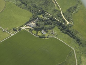 Oblique aerial view centred on the remains of the church and burial ground with the hotel and former manse adjacent, taken from the NE.