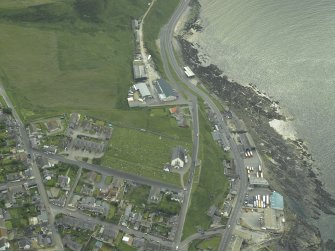 Oblique aerial view centred on the church with the former railway station and fishing station adjacent, taken from the NE.