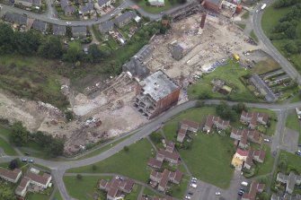 Oblique aerial view centred on the whisky distillery during demolition, taken from the SSW.