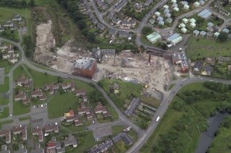 Oblique aerial view centred on the whisky distillery during demolition with the cemetery adjacent, taken from the SE.