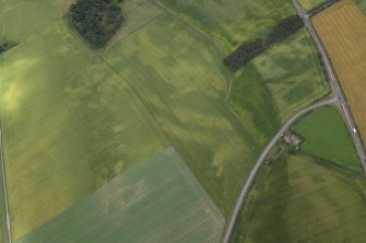 Oblique aerial view centred on the cropmarks of the ring-ditches and roundhouses, taken from the W.