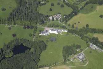 General oblique aerial view centred on the country house, bridge and gardens with the dairy, offices and church adjacent, taken from the SW.