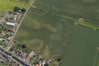 Oblique aerial view centred on the cropmarks of the enclosure and rig with the church adjacent, taken from the NW.