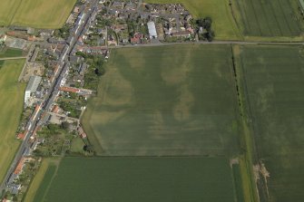 Oblique aerial view centred on the cropmarks of the enclosure and rig with the church adjacent, taken from the WSW.