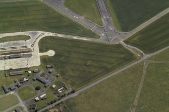 Oblique aerial view centred on the cropmarks of the buildings and the airfield, taken from the NW.