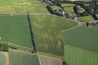 Oblique aerial view centred on the cropmarks of the barrows with the church adjacent, taken from the NNW.