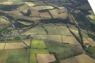 General oblique aerial view centred on the cropmarks of the Roman fort, Roman temporary camps and fort annexes with the village, railway viaduct and road bridge adjacent, taken from the S.