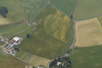 Oblique aerial view centred on the cropmarks of the enclosure, rig and possible settlement with the farmsteading adjacent, taken from the NNW.
