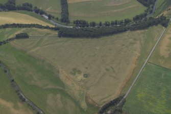 Oblique aerial view centred on the parchmarks of the possible barrows and quarries and the remains of the cairn, taken from the NNE.