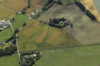 Oblique aerial view centred on the cropmarks of the enclosures and possible building with the manse and remains of the abbey adjacent, taken from the NNE.