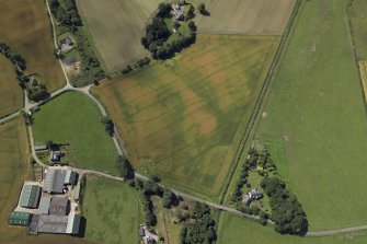 Oblique aerial view centred on the cropmarks of the enclosures and possible building with the manse, farmsteading, farmhouse and remains of the abbey adjacent, taken from the E.