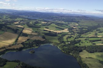 General oblique aerial view looking across the Loch of Clunie towards the Grampian Mountains with the remains of the possible crannog and the church and country house in the foreground, taken from the E.