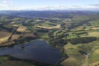 General oblique aerial view looking across the Loch of Clunie towards the Grampian Mountains with the remains of the possible crannog and the church and country house in the foreground, taken from the E.