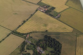 Oblique aerial view centred on the cropmarks of the field boundary and the cropmarks of the quarry with the farmhouse, farmsteading, country house, walled garden and dovecot adjacent, taken from the NW.