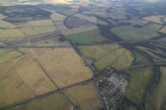 General oblique aerial view centred on the cropmarks of the cursus, ring-ditch, pits and field-system with the country house adjacent, taken from the N.