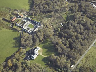 Oblique aerial view centred on the country house, kennels, cottage, farmsteading, byre, farmhouse and walled garden, taken from the WNW.