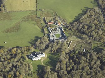Oblique aerial view centred on the country house, kennels, cottage, farmsteading, byre, farmhouse and walled garden, taken from the WSW.
