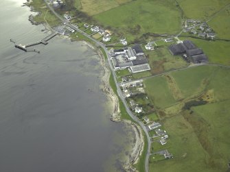 Oblique aerial view of the village centred on the whisky distillery and pier, taken from the NE.