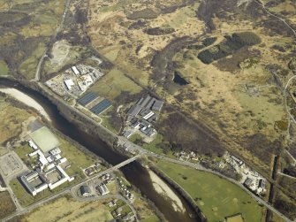 Oblique aerial view centred on the whisky distillery, school and road bridge, taken from the W.