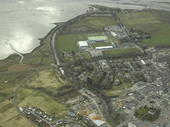 Oblique aerial view of the town centred on the hospital, football ground and stadium with the church in the foreground, taken from the NW.