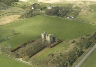 Oblique aerial view centred on the castle with the church, manse, walled garden and remains of the motte adjacent, taken from the E.
