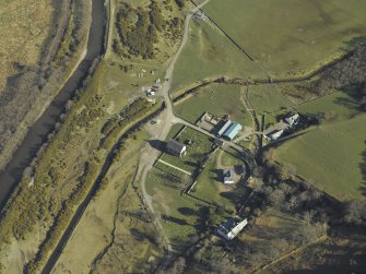 Oblique aerial view centred on the church, burial-ground, manse, road bridge and farmstead, taken from the NW.