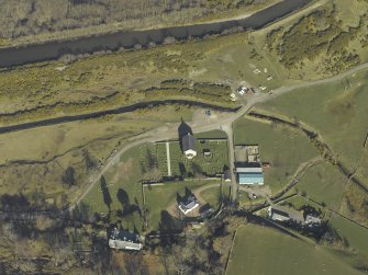 Oblique aerial view centred on the church, burial-ground, manse, road bridge and farmstead, taken from the SW.