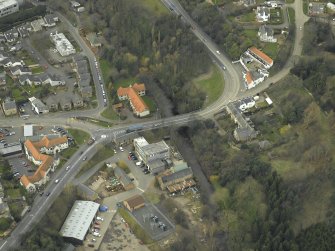 Oblique aerial view centred on the road bridge, abattoir, mill, granary and inn, taken from the E.