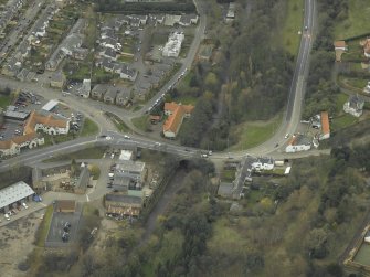 Oblique aerial view centred on the road bridge, abattoir, mill, granary and inn, taken from the ENE.