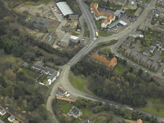 Oblique aerial view centred on the road bridge, abattoir, mill, granary and inn, taken from the NW.