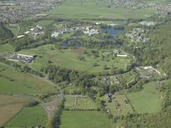 General oblique aerial view centred on the university, library, auditorium, halls of residence, bridge and factory with the church, country house and walled garden in the foreground, taken from the NW.