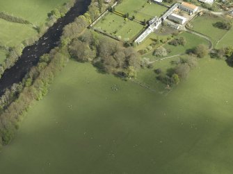 Oblique aerial view centred on the remains of the stone circle with the walled garden, greenhouse, stables and country house adjacent, taken from the SSW.