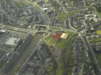 Oblique aerial view centred on the central area of the town, the new leisure Centre on the site of the railway station and the bridges over the River Teviot, taken from the NE.
