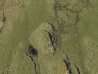 Oblique aerial view centred on the remains of the dun and the shieling huts, taken from the SE.