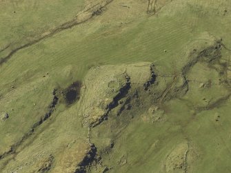 Oblique aerial view centred on the remains of the dun and the shieling huts, taken from the ESE.