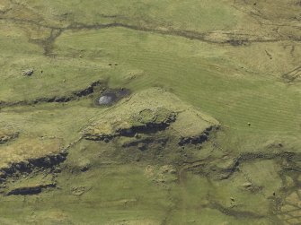 Oblique aerial view centred on the remains of the dun and the shieling huts, taken from the NE.