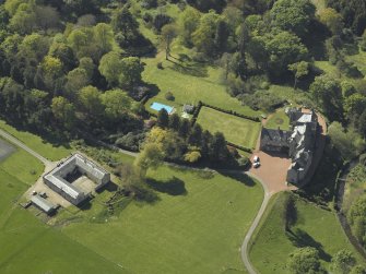 Oblique aerial view centred on the house with the stable block adjacent, taken from the E.