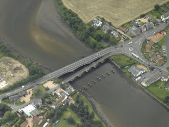 Oblique aerial view centred on the old bridge, rail bridge and new road bridge, taken from the NE.