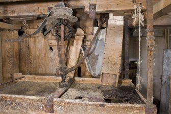 Interior. Ground floor. Sieve, note the shutes from the shelling (left) and the grinding stones (right). Note belt drive from gear cupboard which shakes the sieve which is suspended by leather straps.