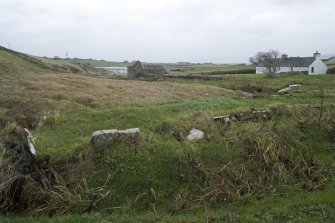 General view looking towards mill building with embanment of dam in foreground. Note up-ended flagstones forming kerb.