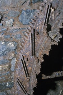 Interior. Detail of inside surface of waterwheel shroud.  Note the cast slots in the wheel rim which took the wooden buckets and the rim spur gear wtith the driven gear above. The remains of the drum boards are visible.