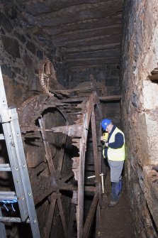 Interior. Waterwheel pit. View of J Borland of RCAHMS undertaking graphic survey. The small driven gear visible.