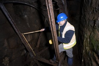 Interior. Waterwheel pit. View of J Borland of RCAHMS undertaking graphic survey. Measuring the waterwheel.